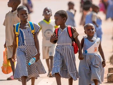 Three young girls in school uniforms walking together outdoors.